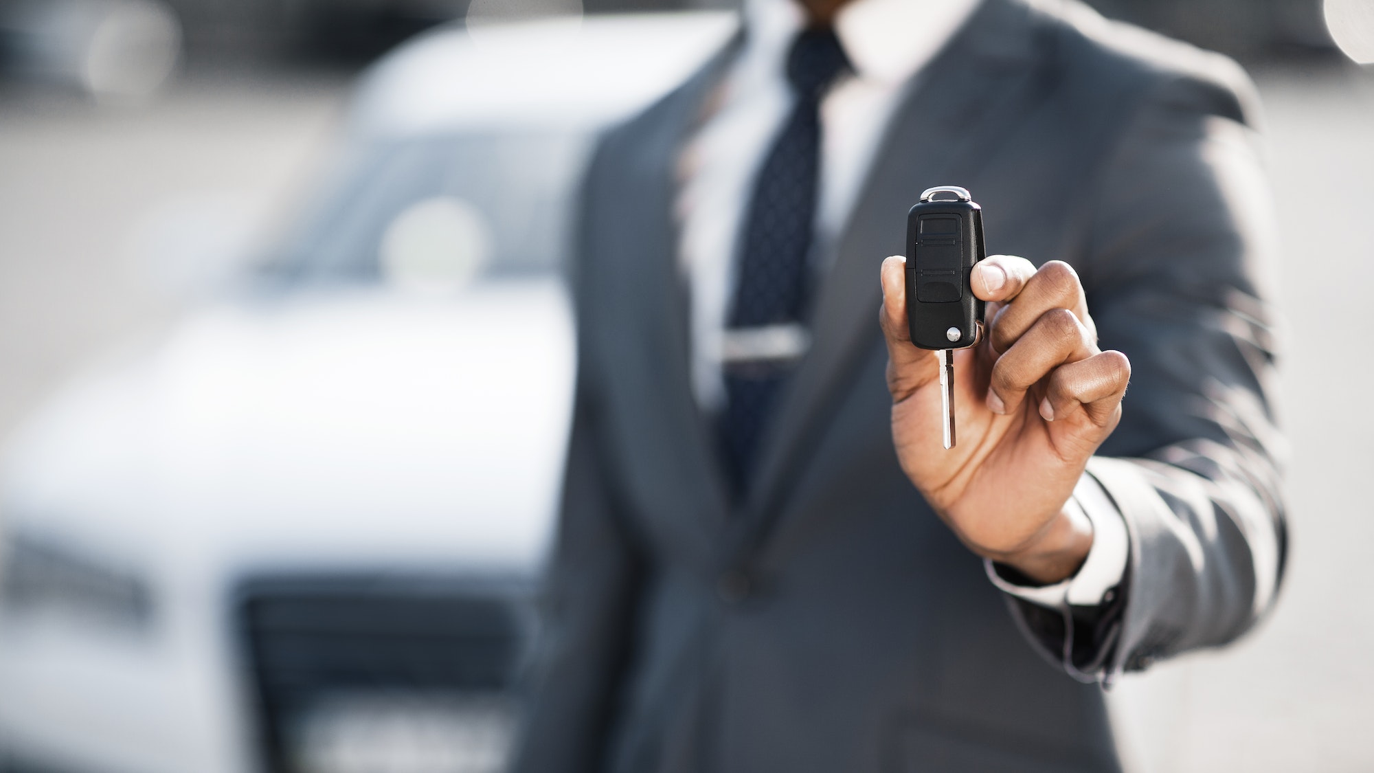 Businessman showing car key against luxury auto